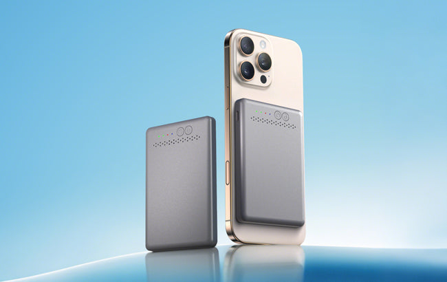 A grey rectangular portable charger standing next to a gold smartphone with an identical charger magnetically attached to its back. Both chargers display small green and red indicator lights and a perforated design. The background is a light blue gradient.