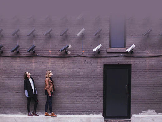 Two women looking up at multiple surveillance cameras mounted on a brick wall.