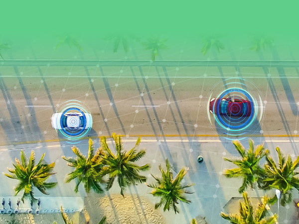 An aerial view of two cars on a coastal road, highlighted with graphics representing sensor technology and connectivity.