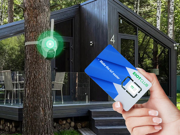 A hand holding an EIOTCLUB SIM card with a security camera mounted on a tree in front of a modern cabin.
