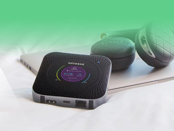 A Netgear mobile hotspot sitting on a laptop next to a pair of headphones.