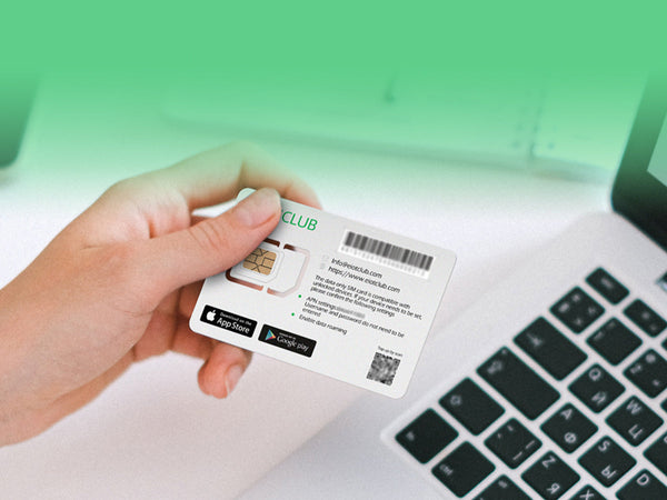 A hand holding a RIOTCLUB SIM card over a laptop keyboard.