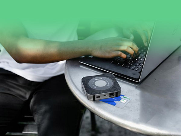 A person working on a laptop, with a portable Wi-Fi hotspot and SIM card on the table.