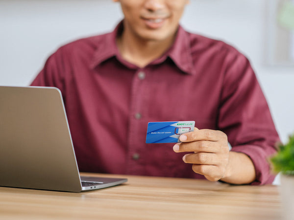 A man holding an EIOTCLUB card while sitting in front of a laptop.